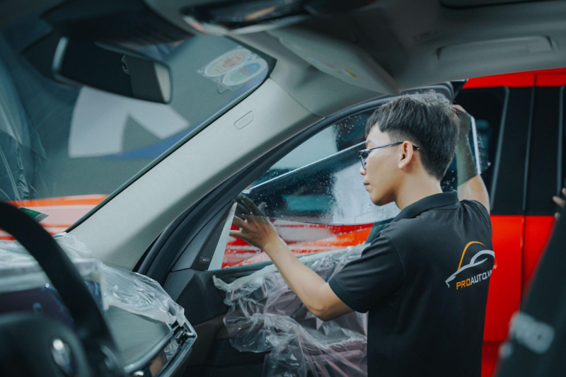 Kỹ thuật viên thi công dán phim cách nhiệt cho kính tài phụ của xe